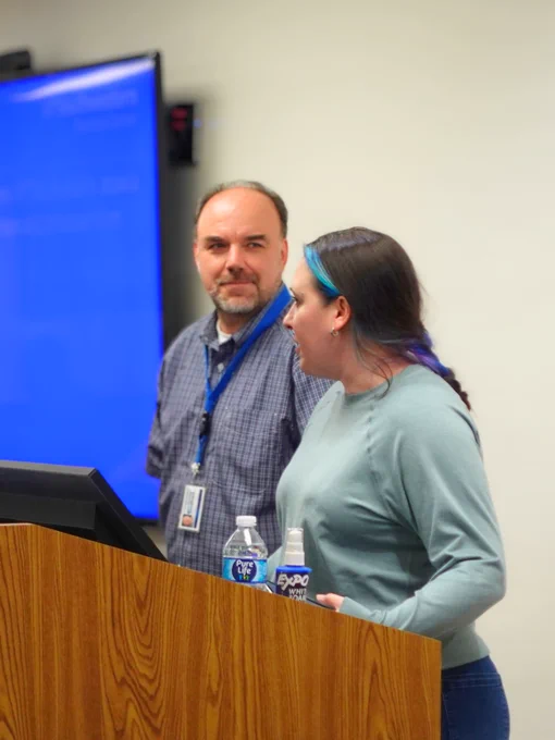 Two people at podium, one speaking one smiling
