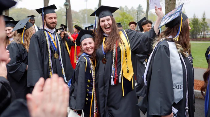 Two graduates smile and celebrate during the procession before Commencement. 