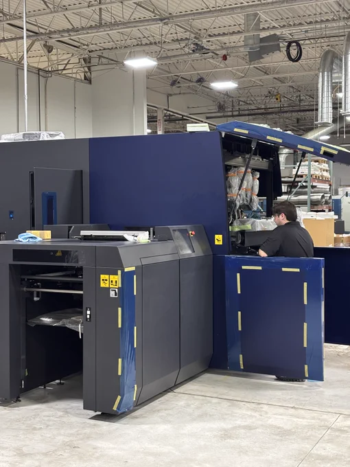 Large blue industrial Accuriojet 30000 Inkjet Press with an open access panel and a technician servicing it in a warehouse