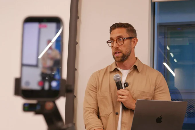 A photo of Paul speaking, with the iPhone recording setup also in view but blurred.