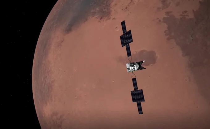 Simulated view of the Psyche spacecraft, with its "wings" of solar panel arrays, passing above the surface of the planet Mars, now seen in nearly full phase.