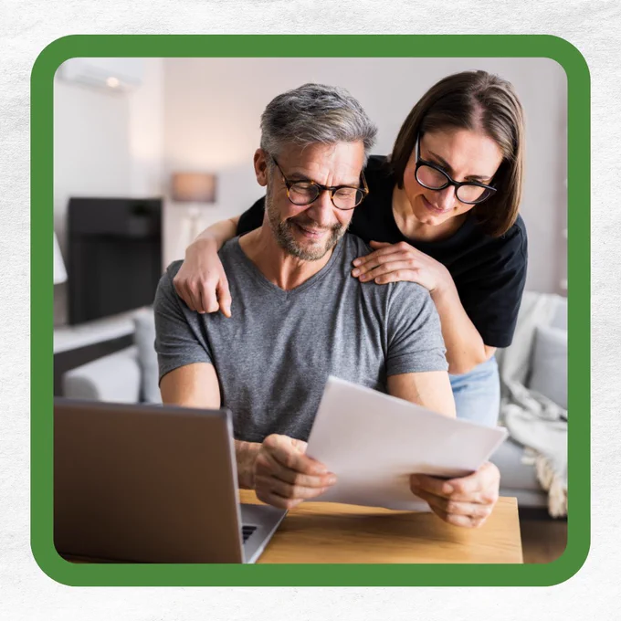 A middle-aged man and a woman look at a piece of paper together in a living room.