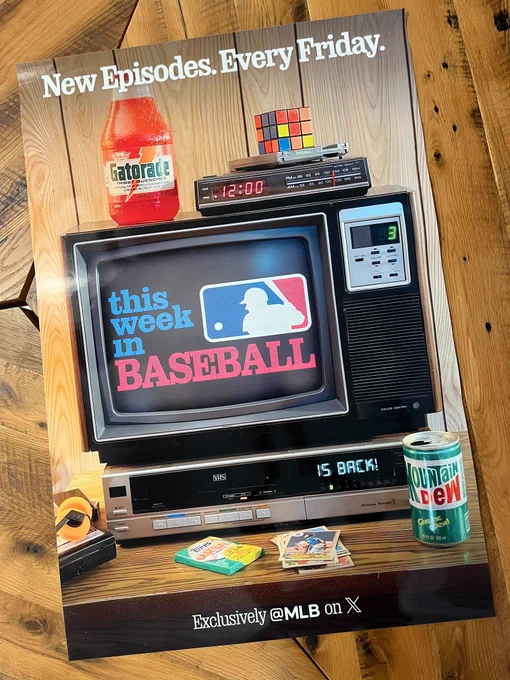A poster laid on a wood table. The poster features a TV on a table with various items reminiscent of the 1990's. The This Week in Baseball logo is on the TV.
