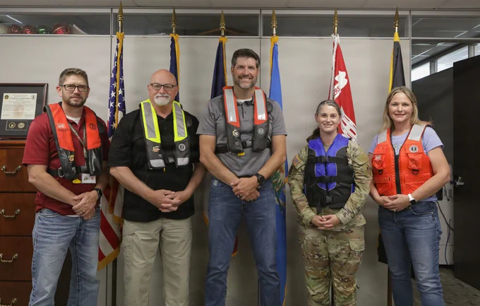 four people in front of flags, wearing life jackets