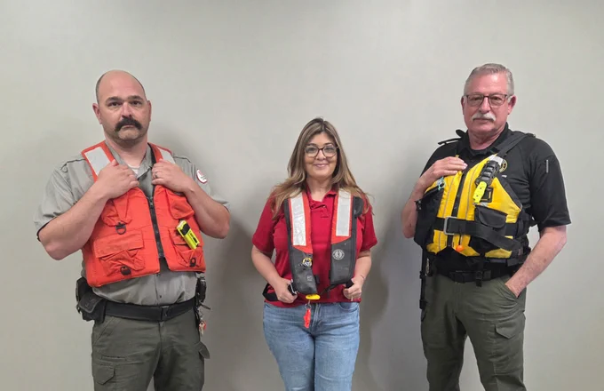 three people standing in front of a wall, wearing life jackets 