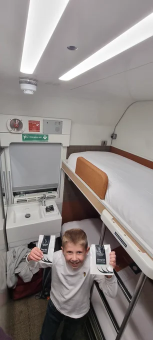 Austin holding some Caledonian Sleeper branded sleep kits. To his left are the bunk beds and behind him is the sink