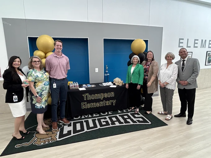 A group of people standing in front of a table displaying the school name and their school mascot logo.