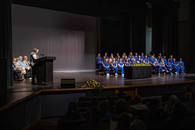 The RSC Nursing graduates are seated on stage while the program director speaks at the podium.