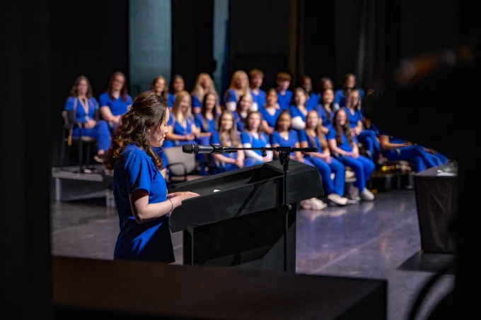 The RSC Nursing graduates are seated on stage while a RSC Nursing student speaks at the podium.