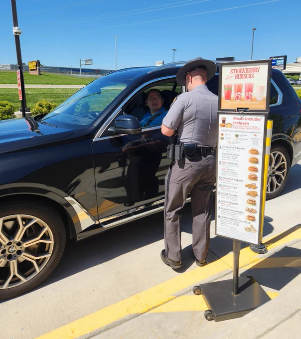 A trooper is discussing traffic safety with a person at in the drive through line during a click it or ticket event. 