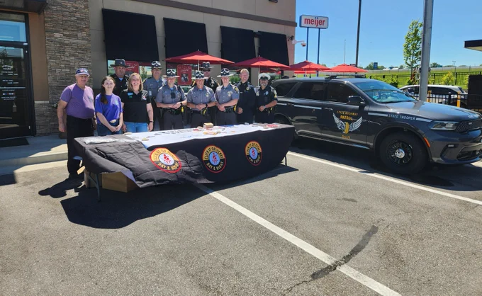 Four troopers and our safety partners stand at a table promoting Click-it or Ticket. A Patrol Durango is parked next to them. 