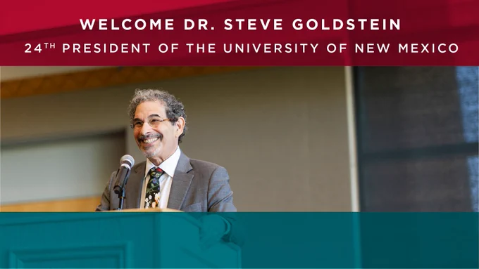 Dr. Steve Goldstein stands at a podium, smiling, with a microphone. Text above reads: "Welcome Dr. Steve Goldstein, 24th President of the University of New Mexico."