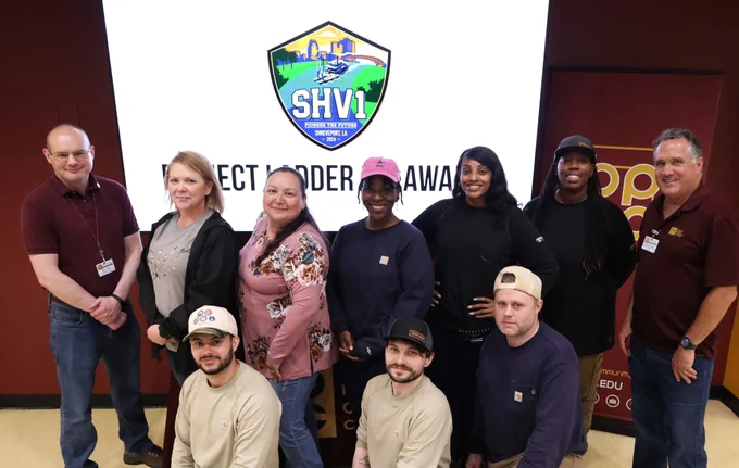 A group of people standing in front of a white wall with a logo and the text "SHV1" logo. 
