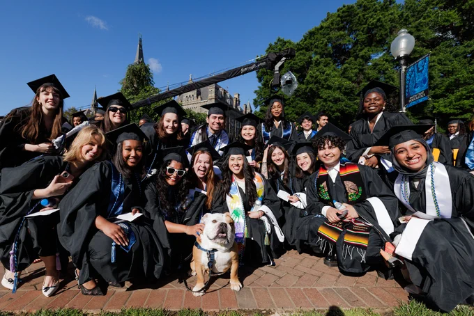A group of students in grad regalia sit with a bulldog