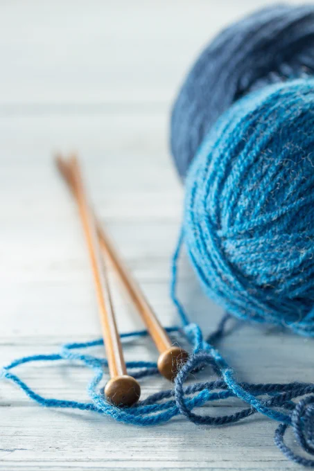 Two wooden knitting needles resting on a white wooden surface with blue yarn balls nearby.

Image credit: [Melica]/ Adobe Stock.