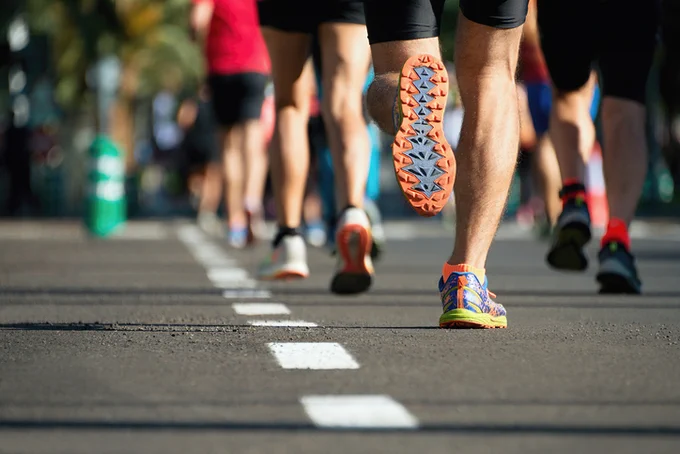 Photograph of crowds of runners on a road taken from the waist down, so only their legs and feet are seen