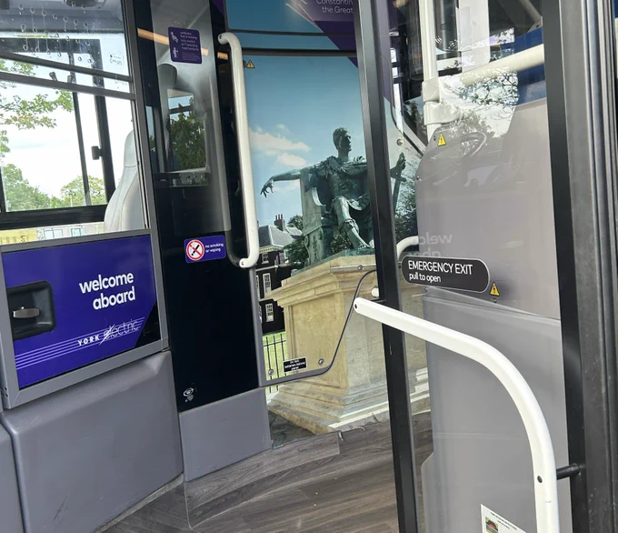 Next to the drivers cab is a full length photo of a York statue on the wall of the bus . A 3D image in. 2D space makes the passage seem wider than it is.