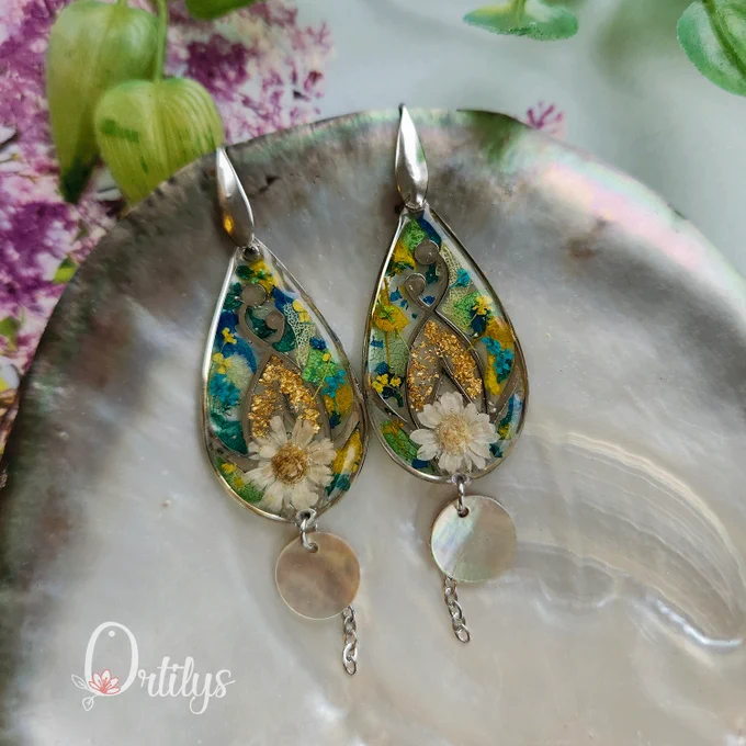 des boucles argentées en forme de goutte, dans les tons blancs, jaunes, bleus et verts. un petit disque de nacre pend des boucles