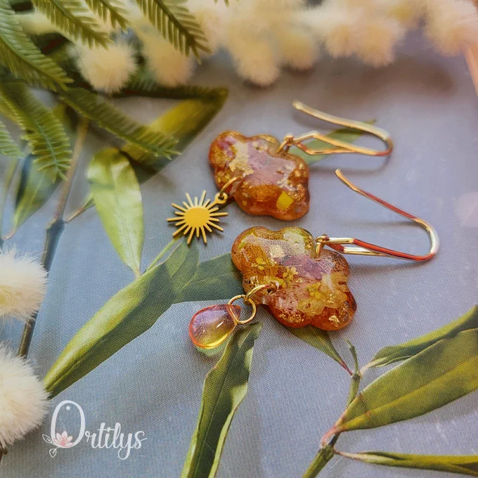 des boucles d'oreilles en forme de nuage, faisant penser au coucher de soleil. elles sont dans les tons orangés dorés et jaunes, un soleil pend d'une boucle, une perle en verre rose orangé pend d'une autre