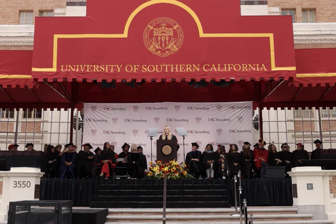Lindsey Vonn stands at a podium between teleprompters in graduation robes during her USC Annenberg commencement address.