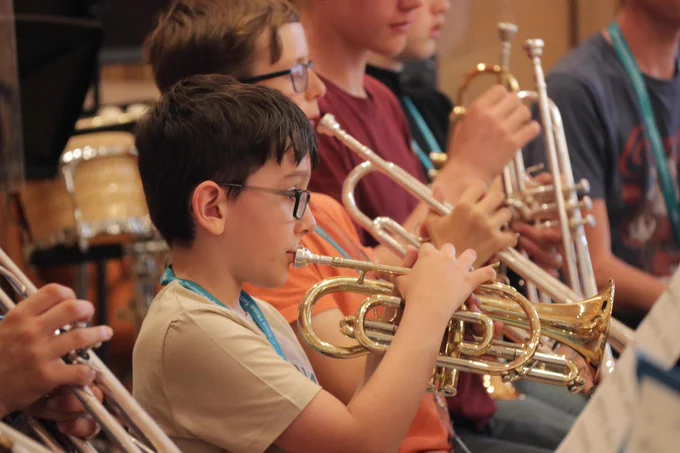 Young musicians seated in a row playing brass trumpets during a band practice session indoors.