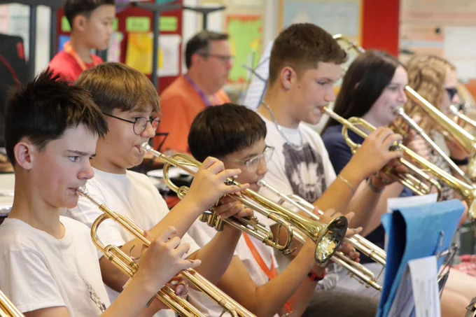 A group of young musicians playing trumpets together in a classroom setting during band practice.