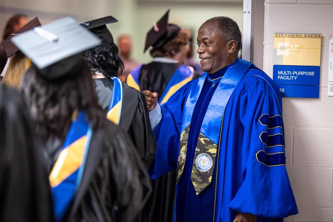 Man is graduation regalia standing backstage congratulating graduates as they walk back.