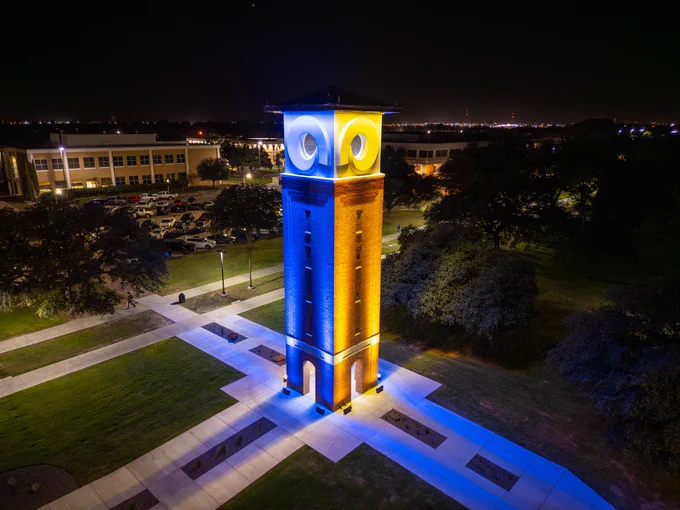 Tower lit blue and yellow at night on a dark college campus.