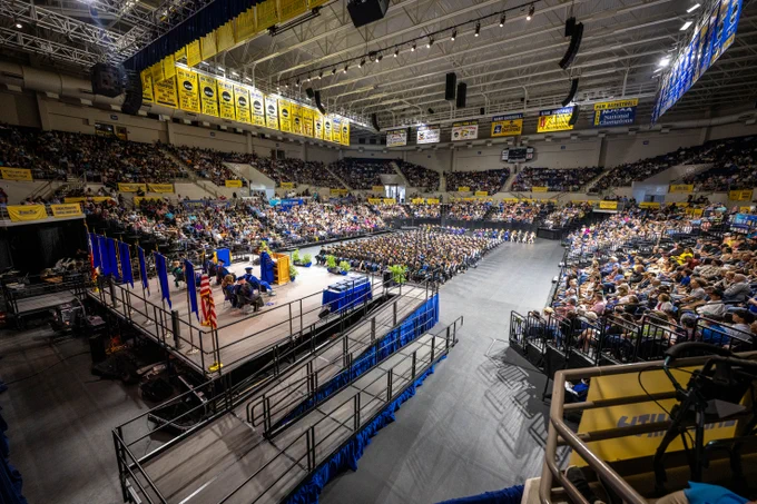 A large indoor arena is filled with people attending a graduation ceremony. 