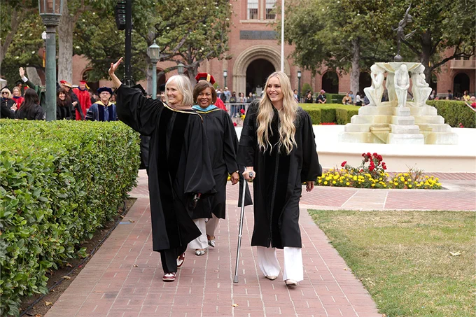 USC Annenberg Dean Willow Bay and Lindsey Vonn lead the faculty processional in academic regalia, smiling and waving to the crowd during USC Annenberg commencement.
