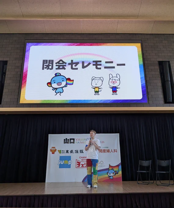 閉会セレモニーの写真。ステージ上で実行委員長がスピーチをしている風景。