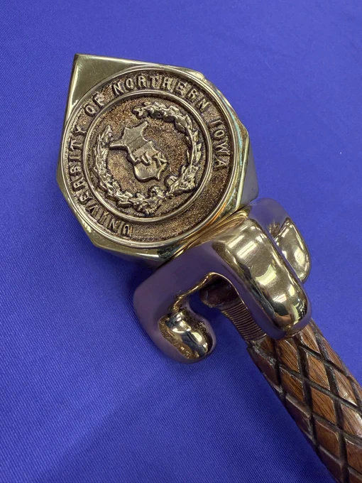 A picture showing the crown of the Centennial Mace, which says “University of Northern Iowa” and shows the Lux symbol