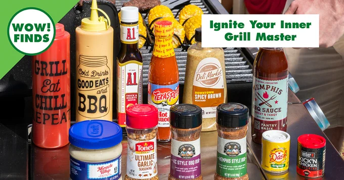 Variety of barbecue sauces, spices, and condiments arranged on a grill with corn and meat in the background.