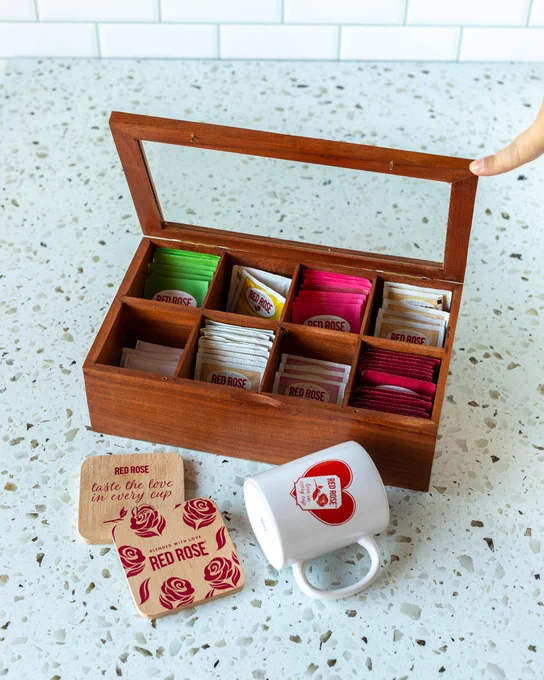 Wooden tea box with compartments holding assorted Red Rose tea bags on a speckled countertop.