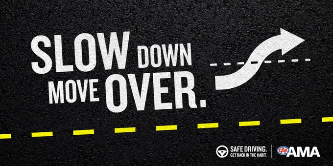 Road safety message painted on asphalt urging drivers to slow down and move over with a curved arrow indicating lane change.