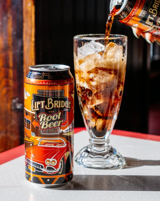 A can of Lift Bridge root beer next to a glass being filled with the soda, set on a retro diner table.
