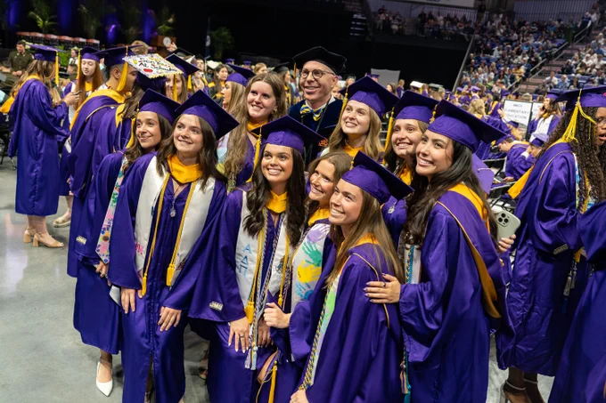 A group of graduates poses for a photo with a faculty member during a commencement ceremony.