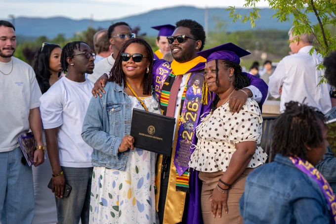 A graduate poses for a photo with family members outside the Atlantic Union Bank Center. One family member is wearing the graduate's cap and the other is holding up a diploma case.