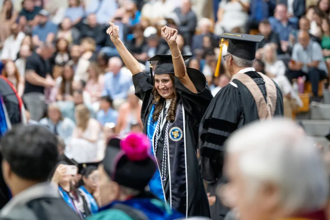 Graduate celebrates while walking across the stage at Commencement.