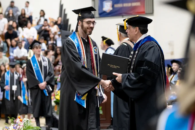 Graduate shakes hands with President Robert Gervasi at Commencement.