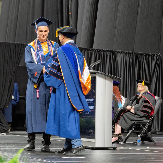Luke Alvarado shakes hands with the dean and is given his diploma.
