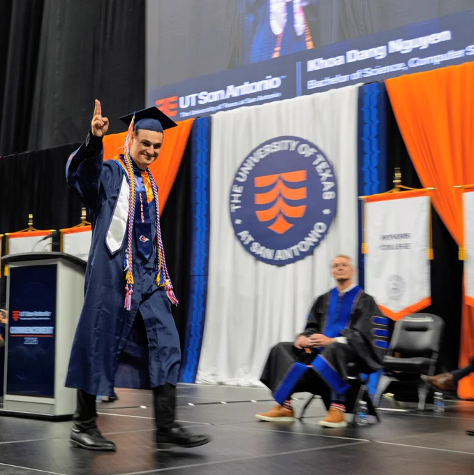 Luke Alvarado waves to the crowd with his degree in hand.