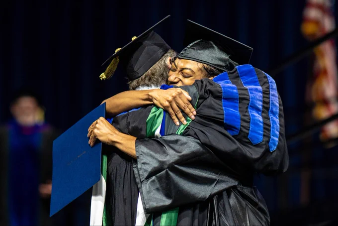 Two individuals embrace at a commencement ceremony.