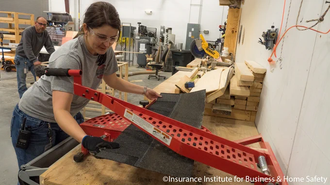 A person is working in a workshop, using a large red tool to cut or shape black material placed on a table. The background shows various woodworking equipment. The space appears organized and well-equipped. © Insurance Institute for Business & Home Safety.