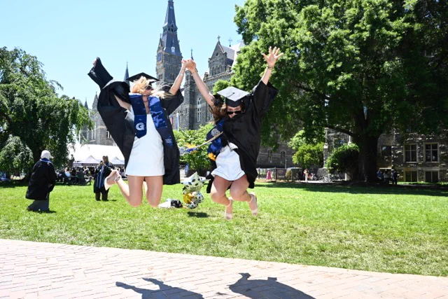 two girls in grad regalia jump