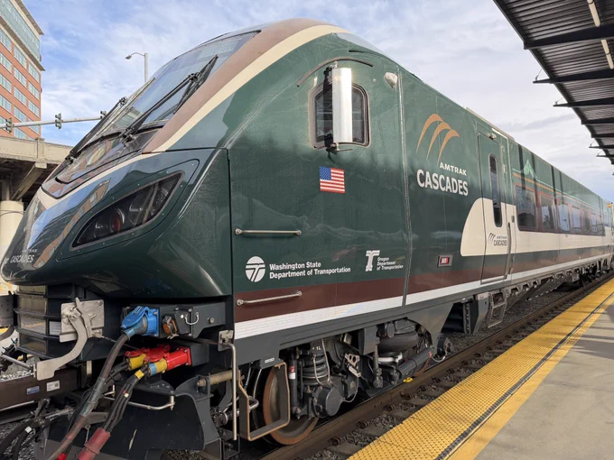 A green passenger train labeled Amtrak cascades sits at a station