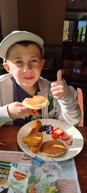 Austin with his plate of breakfast. He has pancakes, strawberries, blueberries, hash browns and sausage