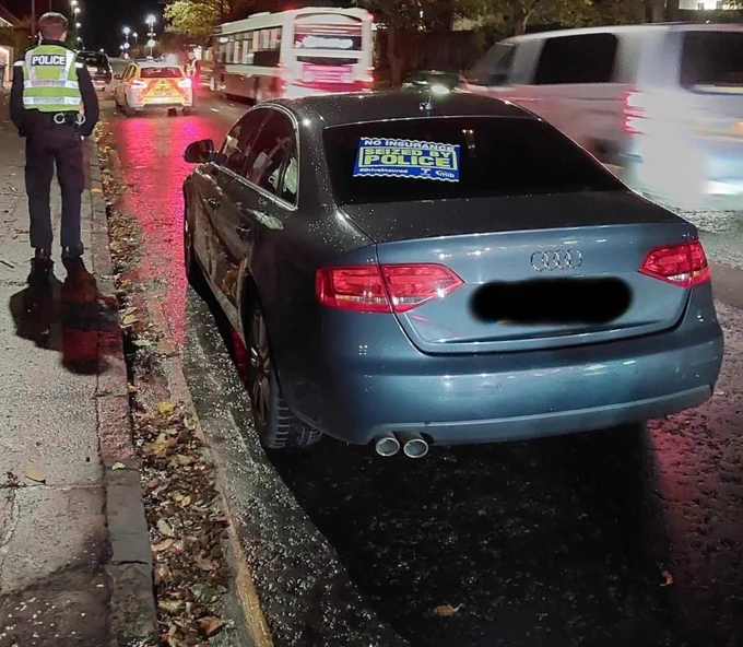 Police officer by a car seized for no insurance, with a warning sticker on the rear window.