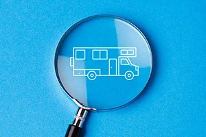 A magnifying glass lies on a blue background, focusing on a simple white line drawing of a recreational vehicle.
