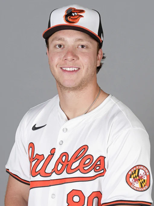 Vance Honeycutt looks at the camera and smiles. He is wearing a white Orioles jersey and a tri-color cap.
